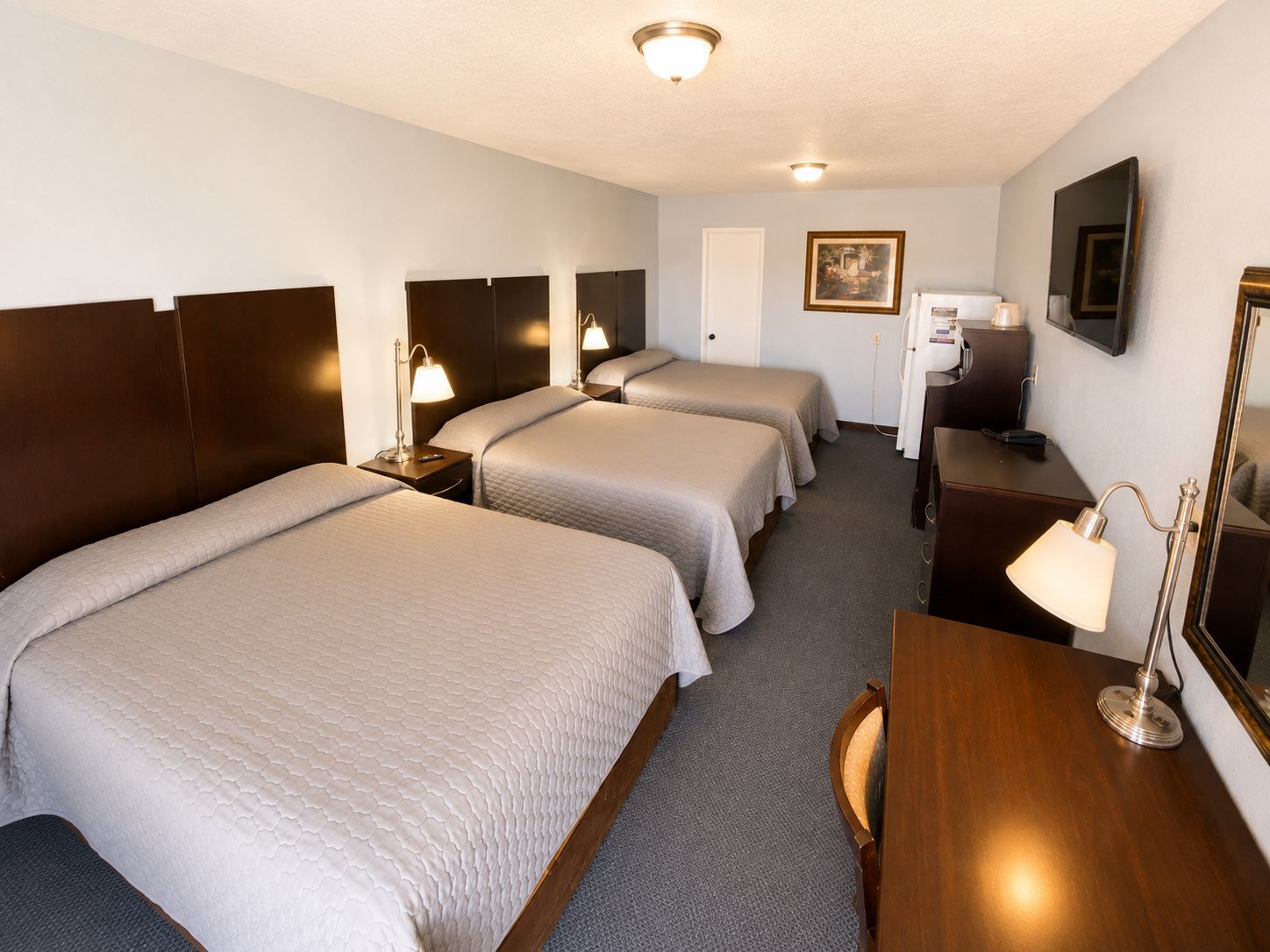 A second Capri Motel triple room with three neatly made beds, a desk, and a television